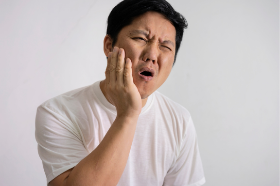 man holds cheek in pain from wisdom teeth